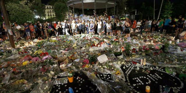 People gather in a new memorial in a gazebo in a seaside park on the famed Promenade des Anglais in Nice, southern France, Monday, July 18, 2016. Mourners formed a human chain to remove flowers, candles and other mementos placed along the Promenade des Anglais as spontaneous memorials to the victims of the Bastille Day attack in preparation to open the westbound lane.(AP Photo/Claude Paris)