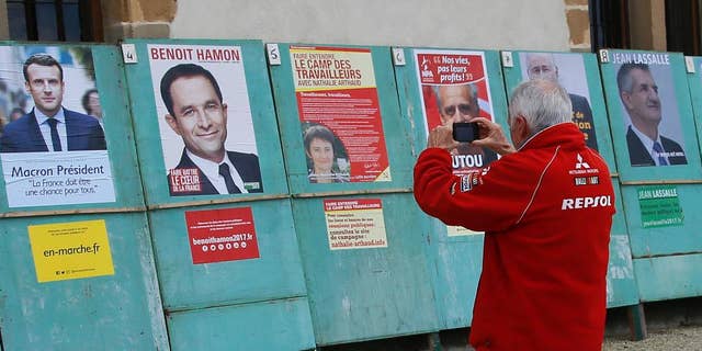 A man takes a picture of electoral posters displaying posters of the presidential candidates in Espelette, southwestern France, Friday, April 14, 2017. The two-round presidential election is set for April 23 and May 7. (AP Photo/Bob Edme)