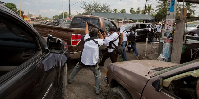 FILE - In this Jan. 12, 2014 file photo, the Self-Defense Council of Michoacan (CAM) engage in a firefight as they try to flush out alleged members of the Knights Templar drug cartel from Nueva Italia, Mexico. The vigilantes say they are liberating territory in the "Tierra Caliente" and are aiming for the farming hub of Apatzingan, said to be the cartel's central command. Mexican military troops stayed outside the town and there were no federal police in sight. (AP Photo/Eduardo Verdugo, File)