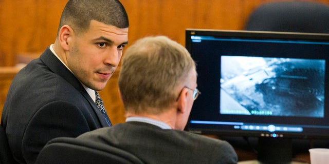 Former NFL player Aaron Hernandez looks at his attorney as security footage is seen on a monitor during his murder trial at the Bristol County Superior Court in Fall River, Mass., Friday, Feb. 20, 2015. Grainy surveillance video shown to jurors in the murder trial of Hernandez on Friday shows the victim an hour before he was killed climbing into a car that prosecutors say was driven by Hernandez. (AP Photo/The Boston Herald, Dominick Reuter)