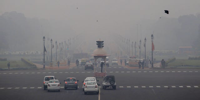Smog and fog envelop the Rajpath, the ceremonial boulevard, behind,  as a police man, center, controls traffic in the morning in New Delhi, India, Wednesday, Feb. 5, 2014. On bad days in India’s congested capital, the air is so murky it slows traffic to a crawl because visibility is so poor. Conversations are punctuated with rasping coughs. Weak bands of sunlight filter through a grainy sky.  (AP Photo/Tsering Topgyal)