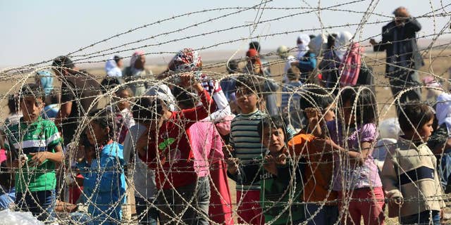 Several hundred Syrian refugees wait to cross into Turkey at the border in Suruc, Turkey, Sunday, Sept. 21, 2014. Turkey opened its border Saturday to allow in up to 60,000 people who massed on the Turkey-Syria border, fleeing the Islamic militants’ advance on Kobani. (AP Photo/Burhan Ozbilici)