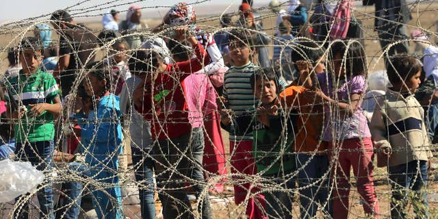 Several hundred Syrian refugees wait to cross into Turkey at the border in Suruc, Turkey, Sunday, Sept. 21, 2014. Turkey opened its border Saturday to allow in up to 60,000 people who massed on the Turkey-Syria border, fleeing the Islamic militants’ advance on Kobani. (AP Photo/Burhan Ozbilici)