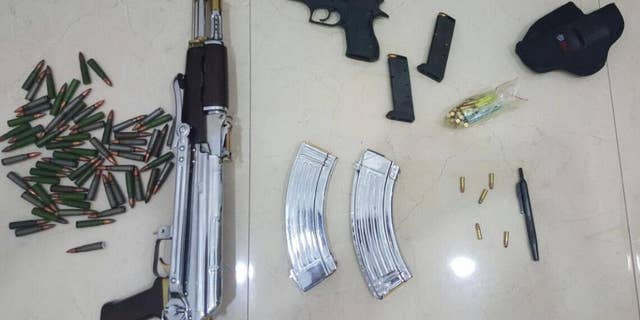 In this Tuesday, June 14, 2016 photo released by the Kuwait Ministry of Interiors, a Kalashnikov rifle, a handgun and ammunition plus a pen gun found and presented after authorities raided the home of Sheikh Athbi al-Fahad Al Sabah the former head of Kuwait's National Security Office, in Kuwait. The hunt for a renegade nephew of Kuwait's emir has turned up a gun disguised as a pen in his home, adding yet another layer of mystery to a bizarre case involving two other ruling family members and others.( Kuwait Ministry of Interiors via AP)