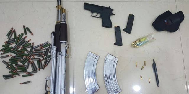 In this Tuesday, June 14, 2016 photo released by the Kuwait Ministry of Interiors, a Kalashnikov rifle, a handgun and ammunition plus a pen gun found and presented after authorities raided the home of Sheikh Athbi al-Fahad Al Sabah the former head of Kuwait's National Security Office, in Kuwait. The hunt for a renegade nephew of Kuwait's emir has turned up a gun disguised as a pen in his home, adding yet another layer of mystery to a bizarre case involving two other ruling family members and others.( Kuwait Ministry of Interiors via AP)