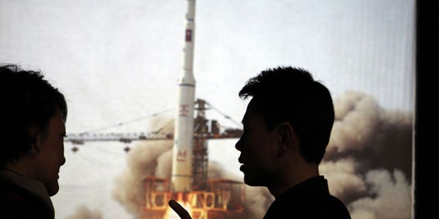 In this photo taken Tuesday, April 10, 2012, North Korean guide Kim Won Ho, right, speaks to a foreign journalist near a photo depicting the 2009 satellite rocket launch at the Three Revolutions exhibition hall in Pyongyang, North Korea.