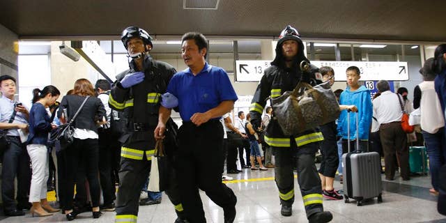 A passenger is escorted by firefighters after getting off a high-speed bullet train where a man set himself of fire, at Odawara station in Odawara, west of Tokyo, Tuesday, June 30, 2015. The man riding one of Japan's high-speed bullet trains set himself on fire Tuesday, killing himself as the coach filled with smoke, Japanese officials and media reports said. (AP Photo/Shizuo Kambayashi)