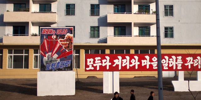 ADDS THE TRANSLATION OF THE POSTER - Morning commuters walk past a poster showing weapons targeting the White House building on a street in Pyongyang, North Korea, Friday, April 19, 2013. The poster reads: "Not by words, but only through arms" (AP Photo/Alexander F. Yuan)
