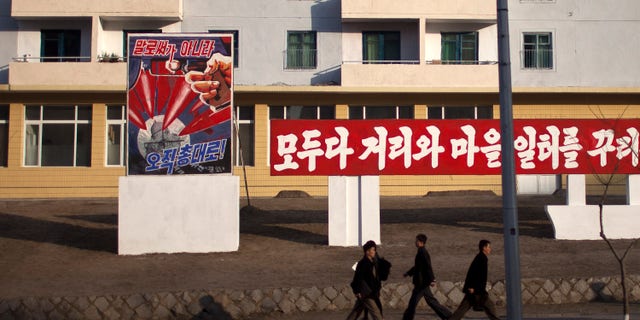 ADDS THE TRANSLATION OF THE POSTER - Morning commuters walk past a poster showing weapons targeting the White House building on a street in Pyongyang, North Korea, Friday, April 19, 2013. The poster reads: "Not by words, but only through arms" (AP Photo/Alexander F. Yuan)