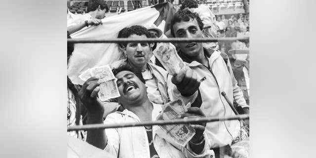 FILE - In this June 25, 1982 file photo, Algerian soccer supporters show money to photographers, in Gijon, Spain, after the World Cup soccer match between West Germany and Austria. On this day: West Germany beat Austria 1-0, a result that meant both teams progressed to the next round at Algeria's expense. After West Germany took an early lead, the game ran its bland course to conclusion to the ire of the watching Algerians. (AP Photo/File)