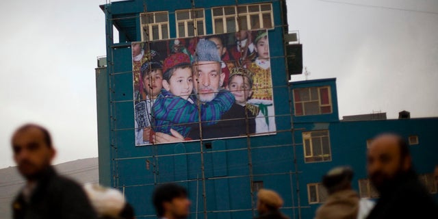 Afghan men waiting to get a ride out of the city line up next to a giant poster of Afghanistan's President Hamid Karzai in Kabul, in 2009.
