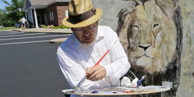 FILE - In this July 29, 2015, file photo, artist Mark Balma paints a mural of Cecil, a well-known lion killed by Minnesota dentist Walter Palmer during a guided bow hunting trip in Zimbabwe, as part of a silent protest outside Palmer's office in Bloomington, Minn. Palmer participated in an interview Sunday, Sept. 6, in which he disputed some accounts of the hunt, expressed agitation at the animosity directed at those close to him and said he would be back at work within days. (AP Photo/Ann Heisenfelt, File)