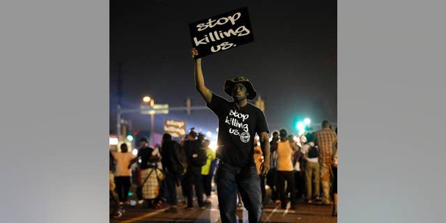 FILE - In this Aug. 18, 2014, file photo, protesters walk through the streets after a standoff with police in Ferguson, Mo. A year ago, most Americans had never heard of the St. Louis suburb called Ferguson. But after a white police officer fatally shot a black 18-year-old in the street, the name of the middle-class community quickly became known around the world. (AP Photo/Charlie Riedel, File)