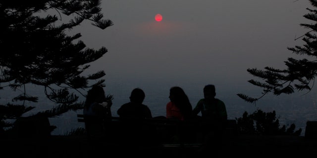 A group of people relax on a park bench at Cerro San Cristobal Park overlooking the Chilean capital which is shrouded by a cloud of smoke from dozens of forest fires that burn near Santiago, Chile, Wednesday Jan. 8, 2014. Residents of Santiago have been suffering from high levels of air pollution caused by the fast-spreading forest fires. The blazes that started over the weekend have caused more than $100 million in property losses. (AP Photo / Luis Hidalgo).