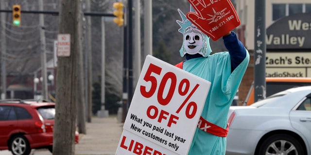 In this March 21, 2015 photo, Brittney Freison, dressed as Lady Liberty, waves to motorists near the Liberty Tax Service office in Berea, Ohio. Wary of rising fees, federal regulators are eyeing ways they can assert tighter oversight upon paid tax preparers who cater to an expanding market of cash-strapped families anxious for their tax refunds. (AP Photo/Mark Duncan)