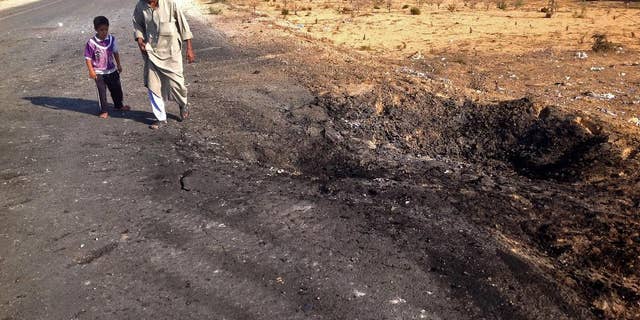 FILE - In this Nov. 20, 2013 file photo, a man and child walk past a crater from a suicide car bomb attack on the road between the border town of Rafah and the coastal city of el-Arish, Egypt. Egyptian authorities on Tuesday, Oct. 28, 2014, ordered residents living along the country's eastern border with the Gaza Strip to evacuate so they can demolish their homes and set up a buffer zone to stop weapons and militant trafficking between Egypt and the Palestinian territory, officials said. The measure comes four days after militants attacked an army post, killing at least 31 soldiers in the restive area in the northeastern corner of the Sinai Peninsula. (AP Photo/Ahmed Abu Deraa, File)