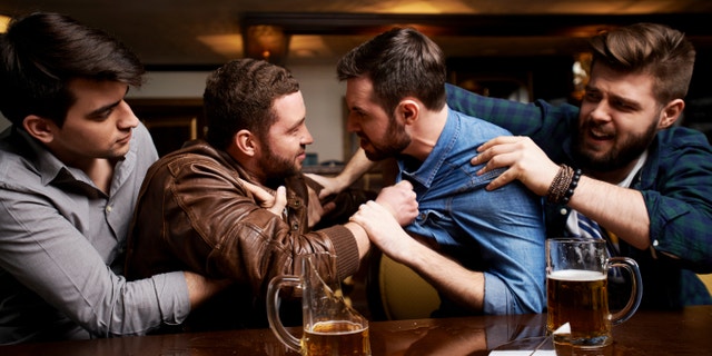 Drunk men fighting in pub, their friends trying to pull them apart, broken beer mug on bar counter