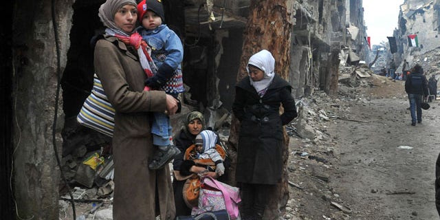 February 4, 2014: In this photo released by the Syrian official news agency SANA, residents of the besieged Yarmouk Palestinian refugee camp wait to leave the camp, on the southern edge of Damascus. Over the past six days the U.N. continued to distribute food parcels in the Palestinian camp where activists say at least 85 people have died as a result of lack of food and medicine since mid-2013. (AP Photo/SANA)