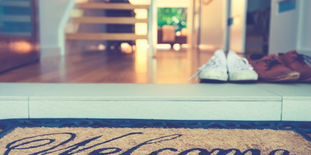 Couples shoes at the front door of a house. There is a welcome mat in the foreground, with a modern home interior in the background. Marriage - home ownership concept