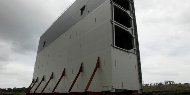 FILE - In this Aug. 22. 2013 file photo, a section of the new rolling gates for the Panama Canal's third set of locks towers over workers during a press tour in Gatun, Panama. The consortium carrying out a historic expansion of the Panama Canal says it may have to suspend work due to financial problems caused by a $1.6 billion cost overrun. The group issued a statement Wednesday, Jan. 1, 2014, giving the Panama Canal Authority 21 days to settle the dispute, but says it will continue working in the meantime. (AP Photo/Arnulfo Franco, File)