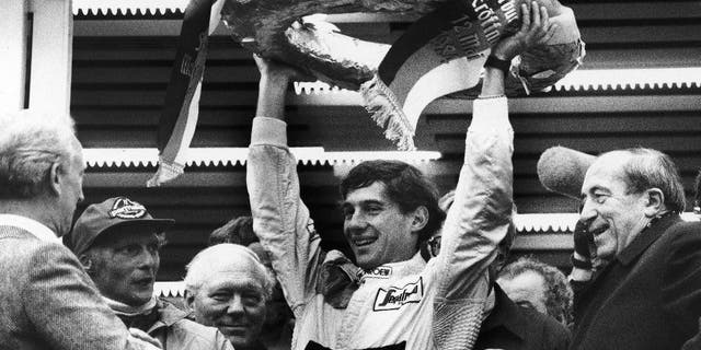 FILE - In this May 13, 1984, file photo, Brazilian Formula One race driver Ayrton Senna da Silva, center, holds up the winner's crown after he won the Mercedes 190 E race in Nuremberg, Germany ahead of former world champion Niki Lauda, second from left. At the right, smiling German transport minister Werner Dollinger. Senna won three Formula One titles — in 1988, 1990 and '91 — all with McLaren. He moved to the Williams team for his tragic 1994 season. Despite his career being cut short when he was 34, his 41 wins stand third all-time behind Michael Schumacher's 91 and rival Alain Prost's 51. He died at the 1994 San Marino Grand Prix. (AP Photo/Udo Weitz, File)