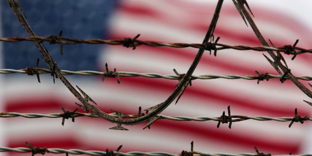 ** FILE ** In this Oct. 10, 2007 file photo, reviewed by the U.S. Military, an American flag flies behind the barbed and razor-wire at the Camp Delta detention facility, at Guantanamo Bay U.S. Naval Base, Cuba. The Pentagon said Saturday that four Afghans from the Guantanamo Bay detention center have been returned to their home country in what U.S. officials are citing as a sign of their confidence in new Afghan President Ashraf Ghani. (AP Photo/Brennan Linsley)