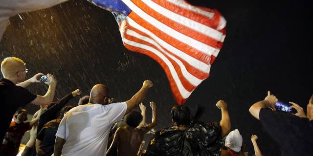Police stand near a suspect in a parking lot after gunfire during a protest on the anniversary of the death of Michael Brown, Sunday, Aug. 9, 2015, in Ferguson, Mo. St. Louis County Police Chief Jon Belmar said that plainclothes officers had been tracking the man, who they believed was armed, during the protest. Belmar said the man opened fire on police and was struck when the officers returned fire. The man was taken to a hospital, where Belmar said he was in surgery early Monday morning. (AP Photo/Jeff Roberson)