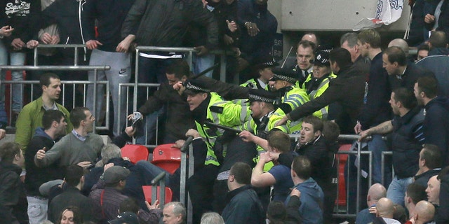 Police officers raise their battens as they control the crowd as Millwall play Wigan Athletic during their English FA Cup semifinal soccer match at Wembley stadium in London, Saturday, April 13, 2013. (AP Photo/Alastair Grant)