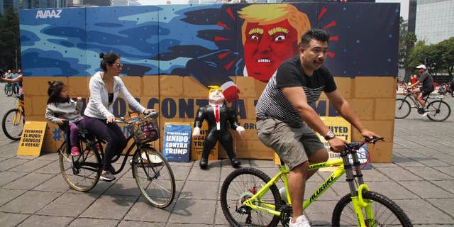 In this Sunday, Sept. 25, 2016 photo, a family of three ride their bicycles past a piñata depicting U.S. Republican presidential nominee Donald Trump propped against a cardboard mural wall with a message in Spanish that reads; "United against Trump" at the Angel of Independence monument in Mexico City. The head of Mexico’s central bank told the Radio Formula network Friday, Sept. 30, 2016, that a Trump presidency “would be a hurricane and a particularly intense one if he fulfills what he has been saying in his campaign.” (AP Photo/Marco Ugarte)
