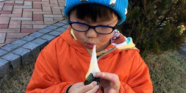 In this Dec. 13, 2014, photo, a boy eats a freshly pounded rice cake, or "mochi," wrapped in a sheet of seasoned laver, or "nori."