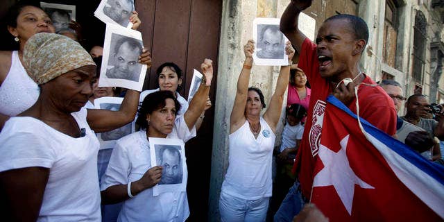 A government supporter, right, chants revolutionary slogans as members of dissident group Ladies in White hold up images of late dissident Orlando Zapata Tamayo on the first anniversary of his death in Havana, Cuba, Wednesday Feb. 23, 2011. Ladies in White is a group of relatives of Cuban dissidents who were or are still imprisoned. (AP Photo/Javier Galeano)