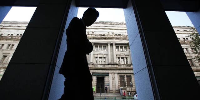 FILE - In this Nov. 19, 2014 file photo, a man walks in front of the Bank of Japan headquarters in Tokyo. Japan's latest data show the economy grew at a real annualized rate of 1.5 percent in October-December, slower than earlier reported but still reaffirming an end to recession. (AP Photo/Shizuo Kambayashi, File)