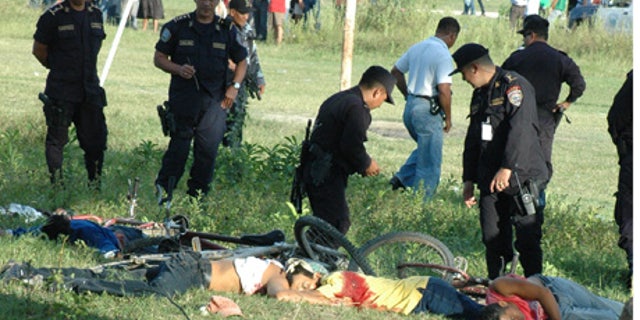 Police officers inspect the bodies of victims of a massacre in a soccer field in San Pedro Sula, Honduras, Saturday Oct. 30, 2010. A carful of attackers armed with assault rifles drove up to the football field Saturday and opened fire, killing at least 14 people.(AP Photo)