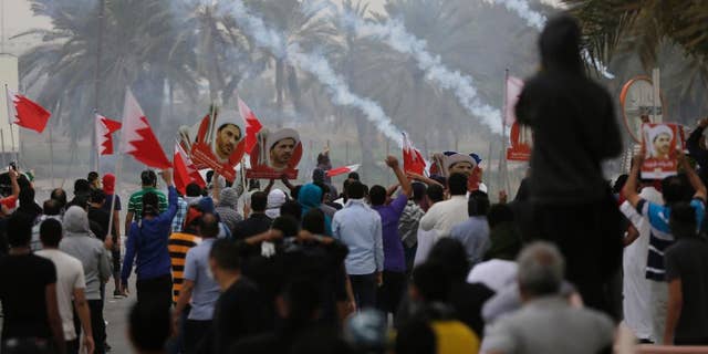 Riot police fire tear gas to disperse Bahraini anti-government protesters waving flags and carrying pictures of jailed Shiite cleric Sheikh Ali Salman, head of the largest opposition political society, Friday, Feb. 13, 2015, in the Manama suburb of Bilad al-Qadeem, Bahrain. Protest marches were held and clashes erupted in opposition areas nationwide Friday, where many shops stayed closed as part of a three-day general strike called by the February 14 opposition youth group before Saturday's fourth anniversary of Bahrain's pro-democracy uprising. (AP Photo/Hasan Jamali)