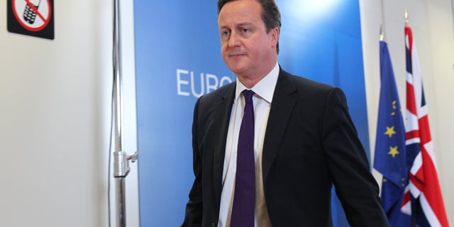 British Prime Minister David Cameron walks past a sign prohibiting the use of mobile phones, after he addressed the media at the European Council building in Brussels, Friday, Oct. 25, 2013. Migration, as well as an upcoming Eastern Partnership summit, tops the agenda in Friday's meeting of EU leaders. (AP Photo/Yves Logghe)