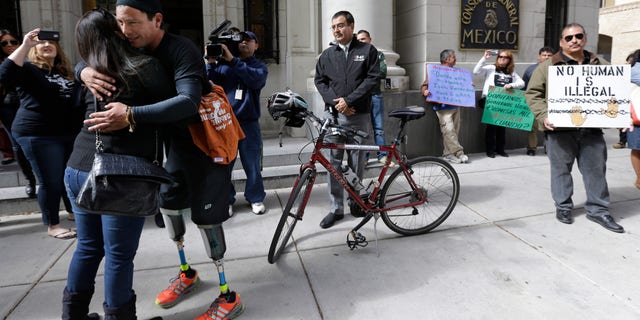 Cyclist Carlos Gutierrez, a double amputee, center, gets a hug from a supporter during a stop at the Mexican Consulate, Thursday, Nov. 7, 2013, in San Antonio. Gutierrez, a Mexican asylum seeker who fled to the U.S. after extortionists cut his legs off for not paying the extortion fees, is riding his bike from El Paso, Texas to Austin, Texas, to raise awareness on the situation of political asylum seekers. (AP Photo/Eric Gay)