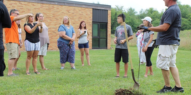 In this Sunday, Aug. 26, 2018, photo classmates that were in the AWARE classes at Coloma Junior High School in 1988 try to find a time capsule that they buried behind the school in Coloma, Mich., that year. The Herald-Palladium reports that the seven classmates and two teachers spent two hours on Sunday digging outside Coloma Junior High in southwestern Michigan.