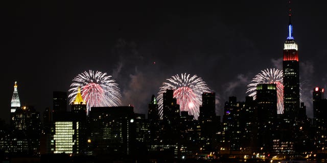 The Empire State Building, illuminated with red, white and blue lights, is seen from the Queens borough of New York, backlit by fireworks over the Hudson River, during the Macy's Fourth of July fireworks show Wednesday, July 4, 2012, in New York. (AP Photo/Frank Franklin II)