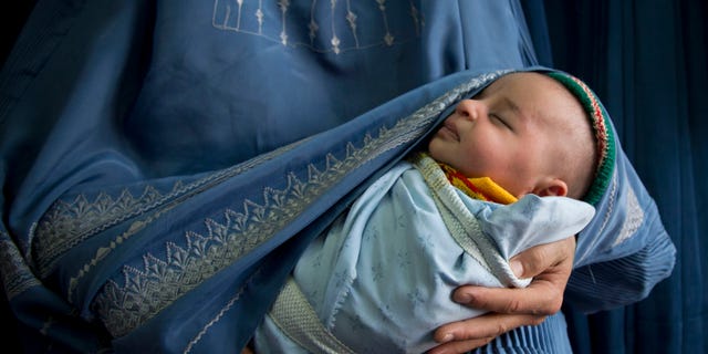 In this Thursday, April 11, 2013 photo, an Afghan woman holds her newly born baby wrapped in her burqa as she waits to get in line to try on a new burqa in a shop in the old town of Kabul, Afghanistan. Despite advances in womens rights, Afghanistan remains a deeply conservative country and most women continue to wear the Burqa. But tradesmen say times are changing in Kabul at least, with demand for burqas declining as young women going to school and taking office jobs refuse to wear the cumbersome garments. (AP Photo/Anja Niedringhaus)