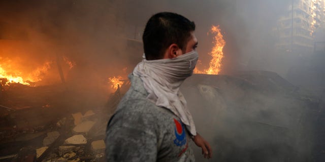 A Hezbollah civil defense worker walks past a burned car at a car bomb in the southern suburb of Beirut, Lebanon, Thursday, Aug. 15, 2013.