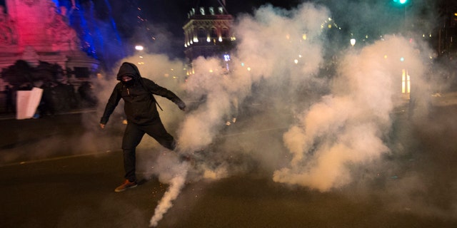 A demonstrator runs away from tear gas during clashes with police in Paris, Sunday, April 23, 2017. Protesters are angry that far-right leader Marine Le Pen is advancing in the French presidential runoff.