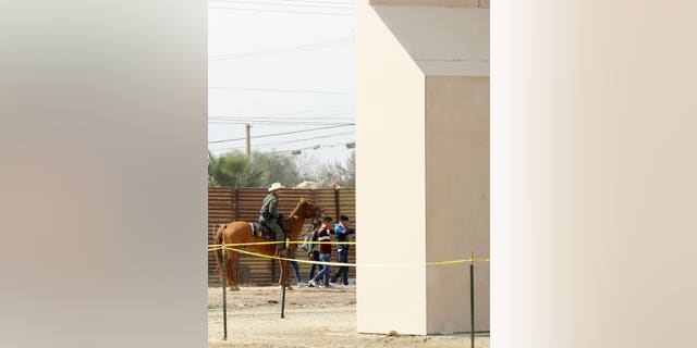 A group of people are detained by Border Patrol agents on horseback after crossing crossing the border illegally from Tijuana, Mexico, near prototypes for a border wall, right, are being constructed Thursday, Oct. 19, 2017, in San Diego. Companies are nearing an Oct. 26 deadline to finish building eight prototypes of President Donald Trump's proposed border wall with Mexico. (AP Photo/Gregory Bull)