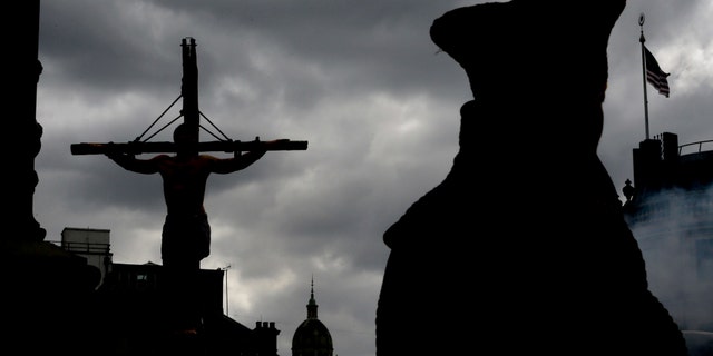 An actor is silhouetted hanging on a cross during a performance in Trafalgar Square in London, Friday, April 18, 2014. The play called 'The Passion of Jesus' was a free performance depicting the betrayal, capture, trial, crucifixion and resurrection of Jesus, performed by the Wintershall players. (AP Photo/Kirsty Wigglesworth)