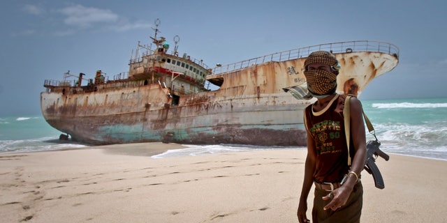 In this photo taken Sunday, Sept. 23, 2012, a masked Somali pirate stands near a Taiwanese fishing vessel that washed up on shore after the pirates were paid a ransom and released the crew, in the once-bustling pirate den of Hobyo, Somalia. Pirates have increasingly turned toward kidnapping because it yields a higher return than selling stolen goods.
