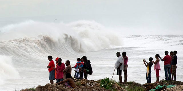 People stand on the coast watching the surf produced by Hurricane Matthew, on the outskirts of Kingston, Jamaica, Monday, Oct. 3, 2016.