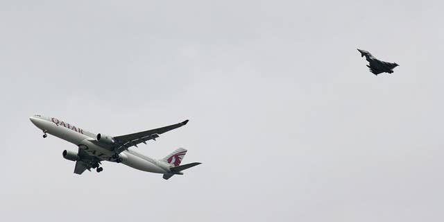 A military fighter jet escorts a passenger jet as it comes in to land at Manchester airport, Manchester, England, Tuesday, Aug. 5, 2014. Police say they have arrested a man on suspicion of making a hoax bomb threat after Qatar Airways Flight 23 landed with a military fighter escort at Britain's Manchester Airport. (AP Photo/Matthew Cossar)