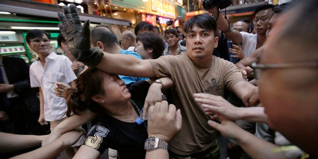 October 4, 2014: A woman is protected from the crowd by pro-democracy student protesters after a scuffle with local residents in Mong Kok, Hong Kong. Friction between pro-democracy protesters and opponents of their weeklong occupation of major Hong Kong streets persisted Saturday as police denied they had any connection to criminal gangs suspected of inciting attacks on largely peaceful demonstrators. (AP Photo/Wally Santana)