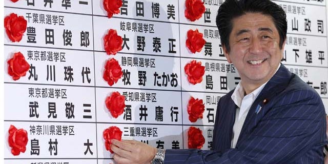 July 21, 2013: Japanese Prime Minister Shinzo Abe smiles as he places a red rosette on the name of his Liberal Democratic Party's winning candidate during ballot counting for the upper house elections at the party headquarters in Tokyo (AP Photo)