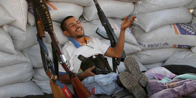 FILE- In this Feb. 9, 2014, file photo, flanked by weapons a man from a self-defense group sits inside a barricade at the entrance of Apatzingan in Michoacan state, Mexico. Vigilantes who have driven a quasi-religious drug cartel from a series of towns in western Mexico entered Apatzingan on Saturday and were working with government forces to clear it of cartel gunmen. The Mexican government announced Tuesday April 15, 2014, that vigilante groups in the western state of Michoacan will have until May 10 to register their guns and decide whether to join the army’s “rural defense corps.” (AP Photo/Marco Ugarte File)
