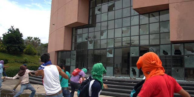 Students from a rural teachers college throw rocks at the entrance to the State Congress after marching through the streets of Chilpancingo, Mexico, Monday Sept. 29, 2014. The students were protesting after a violent weekend left at least 6 people dead and 57 students reported missing. State authorities have confirmed that 22 local policemen have been arrested following the deaths. (AP Photo/Alejandrino Gonzalez)
